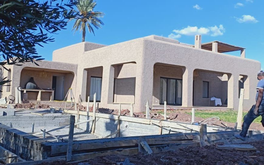 A modern adobe-style house under construction with a partially built structure and scattered construction materials.