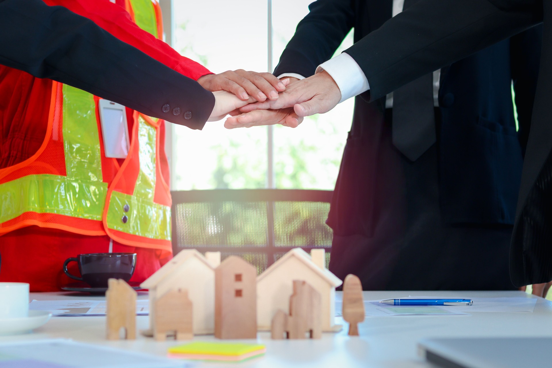 Hommes d’affaires et ingénieurs se donnant la main sur le bureau de réunion, ayant un document de contrat papier, un plan et une maison modèle sur la table, un partenariat se tenant la main, un travail d’équipe d’unité Concept de main jointe.