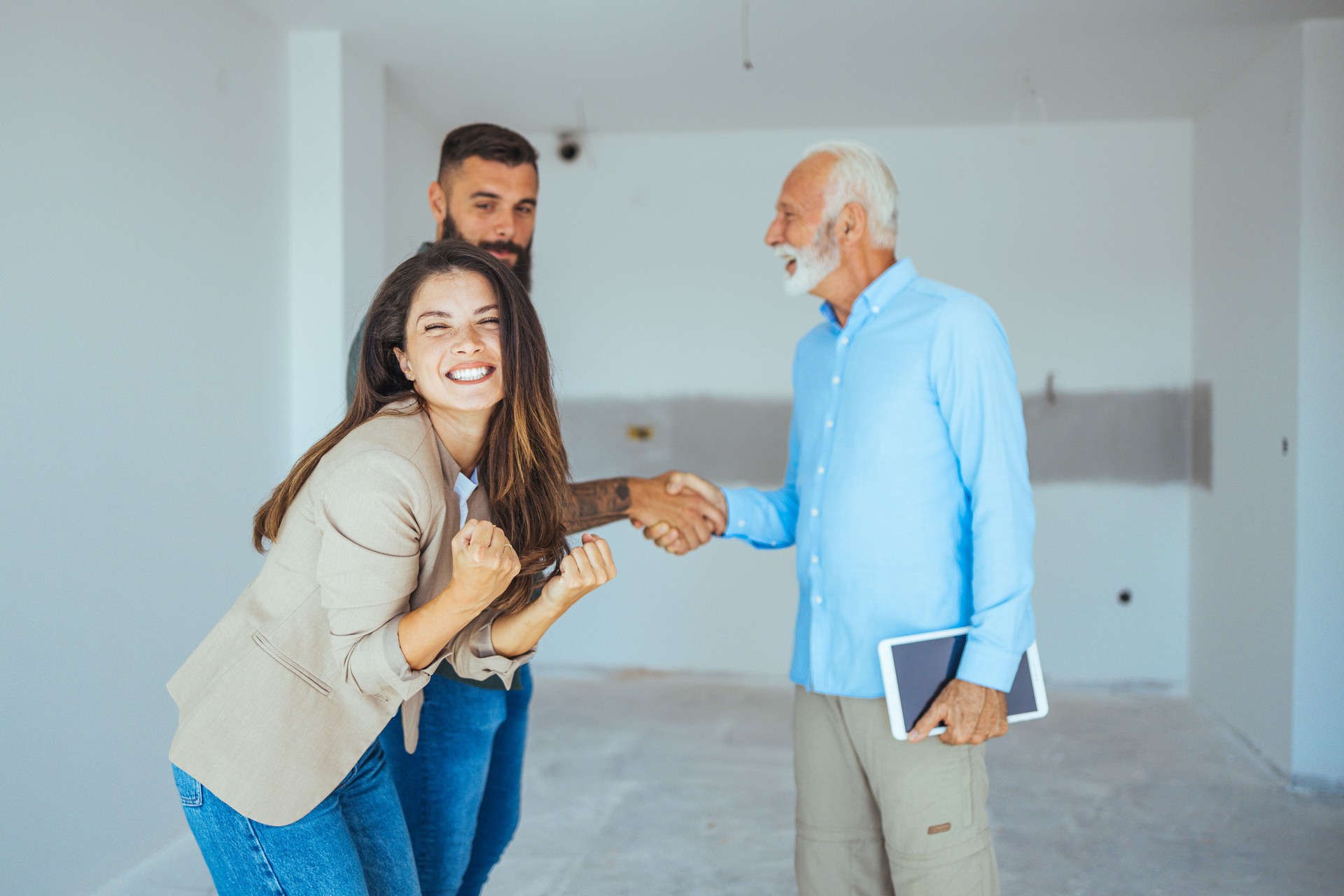 Agent immobilier montrant une maison en construction à un couple et les saluant avec une poignée de main sur un chantier de construction.